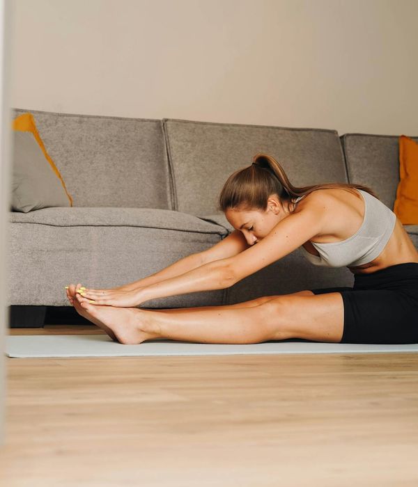 Woman performing a gentle yoga stretch in a dark room with golden light.